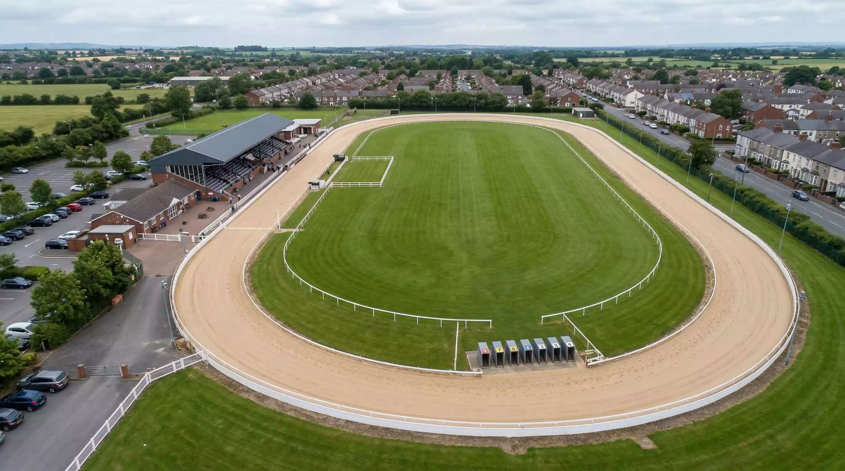 Aerial view of a greyhound racing oval track with sand surface showing the bend layout and starting traps